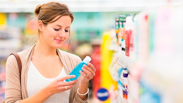 Frau blickt prüfend auf ein Kosmetikprodukt im Drogeriemarkt. | Bild: mauritius images