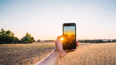 Mann fotografiert Sonnenaufgang mit seinem Handy | Bild: mauritius images