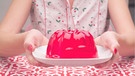 Frau hält einen Teller mit rotem Wackelpudding darauf in den Händen | Bild: mauritius images