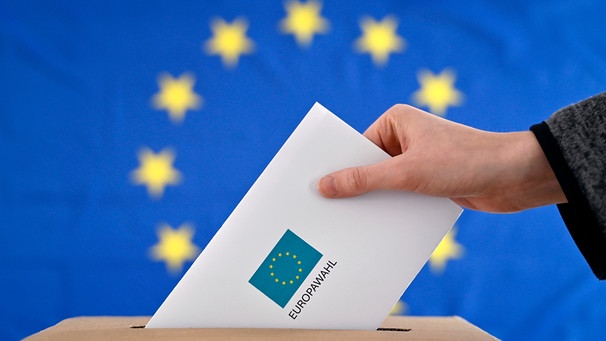 Eine Hand schiebt einen Wahlschein in eine Urne, auf den "Europawahl 2024" gedruckt ist - Symbolbild | Bild: picture alliance / Panama Pictures | Dwi Anoraganingrum