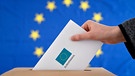 Eine Hand schiebt einen Wahlschein in eine Urne, auf den "Europawahl 2024" gedruckt ist - Symbolbild | Bild: picture alliance / Panama Pictures | Dwi Anoraganingrum