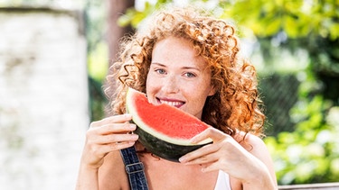 Eine Frau hält ein Stück Wassermelone in den Händen und lächelt. | Bild: mauritius-images