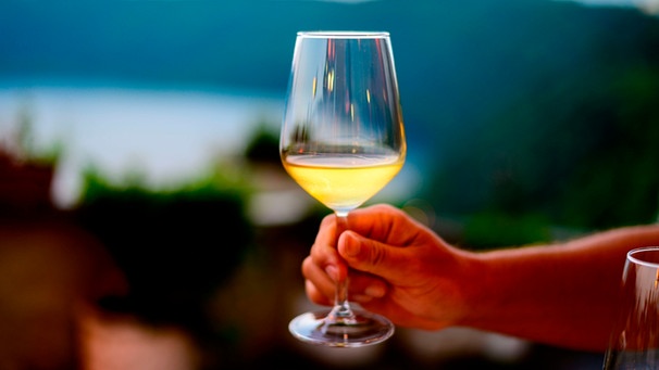 Eine Hand hält ein Weißweinglas in der Hand in einer Abendstimmung. | Bild: mauritius images / Irina Naoumova / Alamy / Alamy Stock Photos