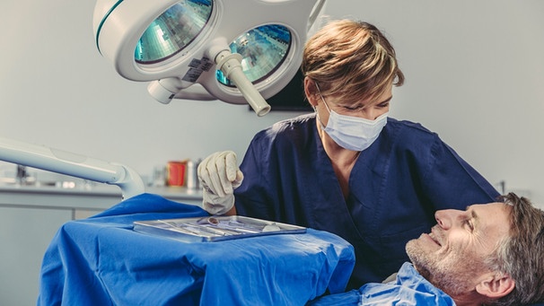 Eine Zahnärztin lächelt ihren Patienten auf dem Behandlungstuhl an. | Bild: mauritius images