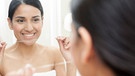 Frau im Badezimmer hält Zahnseide in den Händen. | Bild: mauritius images