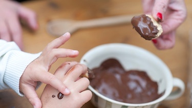 Familie beim Backen von Plätzchen mit flüssiger Schokolade, man sieht nur die Hände der Miutter und des Kindes, wie sie Plätzchen eintunken | Bild: mauritius images