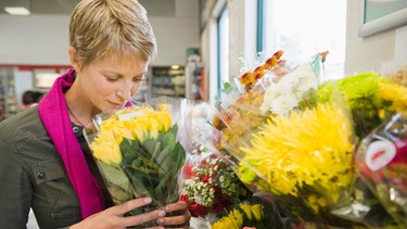 Kurzhaarige Frau schnuppert an Blumen im Supermarkt | Bild: mauritius-images