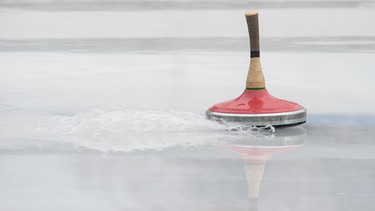 Ein roter Eisstock flitzt über das nasse Eis. | Bild: picture-alliance/dpa/Rainer Jensen