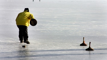 Ein Mann trainiert auf dem zugefrorenen Chiemsee das Eisstockschießen. | Bild: picture-alliance/dpa/Paul Mayall D2253
