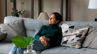 Eine Frau sitzt auf einem Sofa in einem Wohnzimmer | Bild: mauritius images