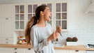 Gut gelaunt singt eine junge Frau in der Küche und nutzt den Schneebesen als imaginäres Mikrofon | Bild: mauritius images / Alamy Stock Photos / Aleksandr Davydov