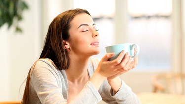 Frau hält eine Tasse mit Kaffee in den Händen und genießt sie mit geschlossenen Augen | Bild: mauritius images