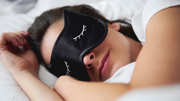 Frau liegt in einem Bett und schläft mit einer Schlafmaske | Bild: mauritius images