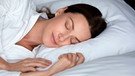 Eine Frau liegt in einem Bett und schläft mit einem Lächeln auf den Lippen | Bild: mauritius images