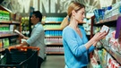 Eine Frau hält in einem Supermarkt eine Packung in der Hand und prüft die Angaben | Bild: mauritius images / Alamy Stock Photos / Liubomyr Vorona