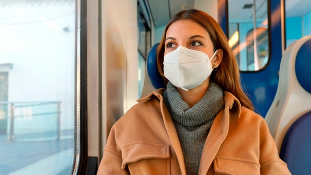 Eine Frau sitzt in einem Zug und trägt eine FFP2-Maske | Bild: mauritius images