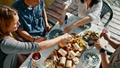 Freunde sitzen zusammen und essen Käse an einem Tisch an einem See | Bild: mauritius images