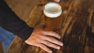 Ein Glas alkoholfreies Weißbier steht auf einem Tresen neben der Hand eines Mannes | Bild: mauritius images