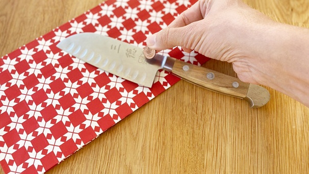 Eine Hand legt einen Cent auf ein Messer neben einer Geschenkverpackung | Bild: BR