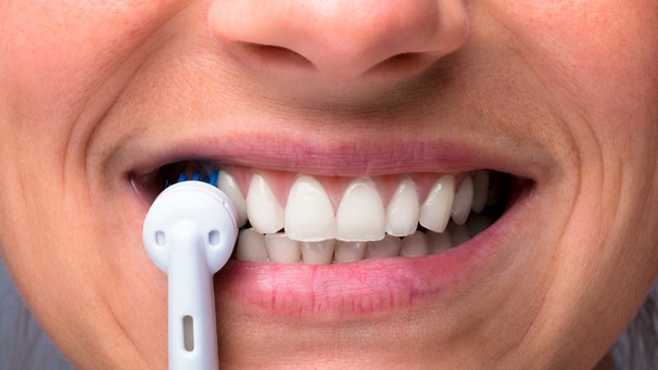 Eine elektrische Zahnbürste vor einem Mund | Bild: mauritius images