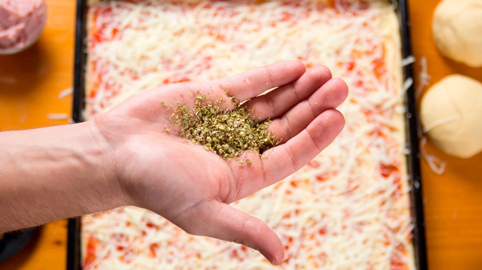 Getrockneter Oregano liegt in einer Hand, darunter ein Blech mit Pizza | Bild: mauritius images Aleksandar Tomic