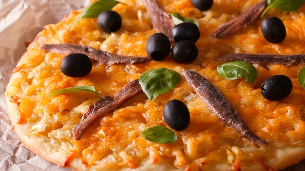 Eine Pizza mit Sardellenfilets, schwarzen Oliven, Käse und Basilikumblättern liegt auf Backpapier | Bild: mauritius images / Sergii Koval / Alamy / Alamy Stock Photos