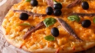 Eine Pizza mit Sardellenfilets, schwarzen Oliven, Käse und Basilikumblättern liegt auf Backpapier | Bild: mauritius images / Sergii Koval / Alamy / Alamy Stock Photos