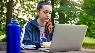 Eine Schülerin sitzt mit einem Laptop im Park | Bild: mauritius images / Image Source / Bruno Gori