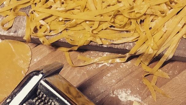 Selbstgemachte Tagliatelle liegen auf einem Holzbrett, daneben ist eine manuelle Nudelmaschine zu sehen | Bild: BR/ Susanne Wolff