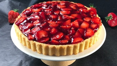 Ein Tortenboden mit saftig glänzenden Erdbeeren belegt auf einer Kuchenplatte | Bild: BR