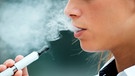 Eine Nahauzfnahme eienr jungen frau, die eine E-Zigarette raucht, mit der typischen Rauchentwicklung | Bild: mauritius-images