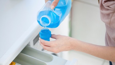 Frauenhand füllt Flüssigwaschmittel in einen Dosierbecher vor dem Spülfach einer Waschmaschine | Bild: mauritius images / pa / Christin Klose