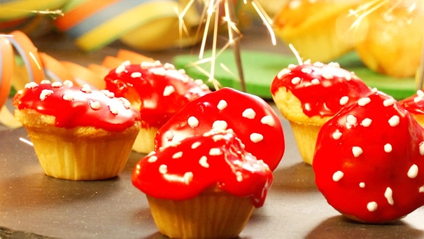 Muffins mit rotem Zuckerguss und weißen Tupfen liegen auf einer Schieferplatte | Bild: BR
