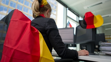 Eine Frau sitzt an einem mit Deutschlandfahnen dekorierten Schreibtisch. | Bild: picture-alliance/dpa