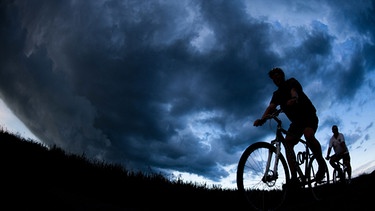 Zwei Radfahrer vor Gewitterwolke | Bild: picture-alliance/dpa