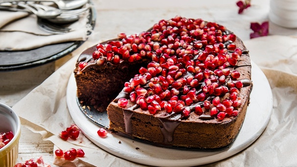 Ein herzförmiger Schokokuchen in Herzform garniert mit Granatapfelkernen ist auf einem Tisch angerichtet. | Bild: mauritius-images