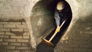 Kanalarbeiter reinigt einen Schacht mit einem Besen | Bild: Imago/Blickwinkel