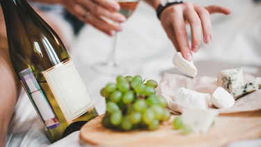 Appetitlicher Käse auf einem Brett, daneben ein Glas Wein | Bild: mauritius-images