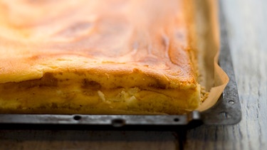 Auf einem Backblech liegt ein fertig gebackener Käsekuchen. | Bild: mauritius-images