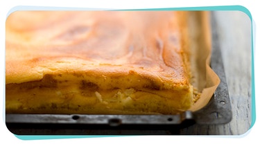 Auf einem Backblech liegt ein fertig gebackener Käsekuchen. | Bild: mauritius images / foodcollection