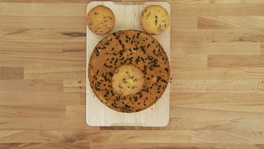 Ein Muffin liegt auf dem Kuchen, die anderen beiden oberhalb davon.  | Bild: BR