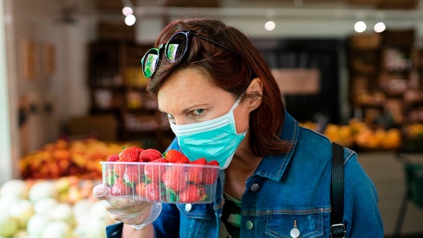 Frau mit Mundschutz begutachtet Erdbeeren | Bild: mauritius-images