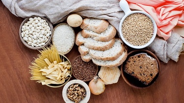 Kohlehydrat -haltige Lebensmittel wie Brot und Nudeln auf einem Holzbrett | Bild: mauritius-images