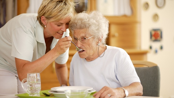 Pflegerin hilft älterer Dame beim Essen | Bild: mauritius-images