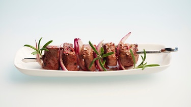Auf einem weißen Teller liegt ein Schaschlikspieß mit Fleisch und roten Zwiebeln | Bild: mauritius-images