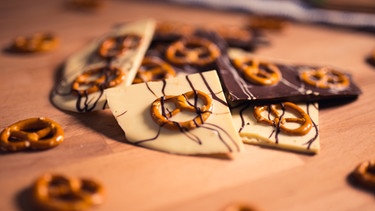 Die fertige mit Salzbrezn verzierte Bruchschokolade liegt auf einem Holzbrett.  | Bild: BR/Anna Ellmann