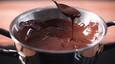 Flüssige dunkle Schokolade tropft von einem Löffel in eine Schüssel.  | Bild: BR/Anna Ellmann