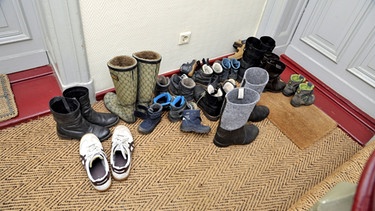 Schuhe stehen auf dem Treppenabsatz vor einer Wohnungstür. | Bild: picture-alliance/dpa