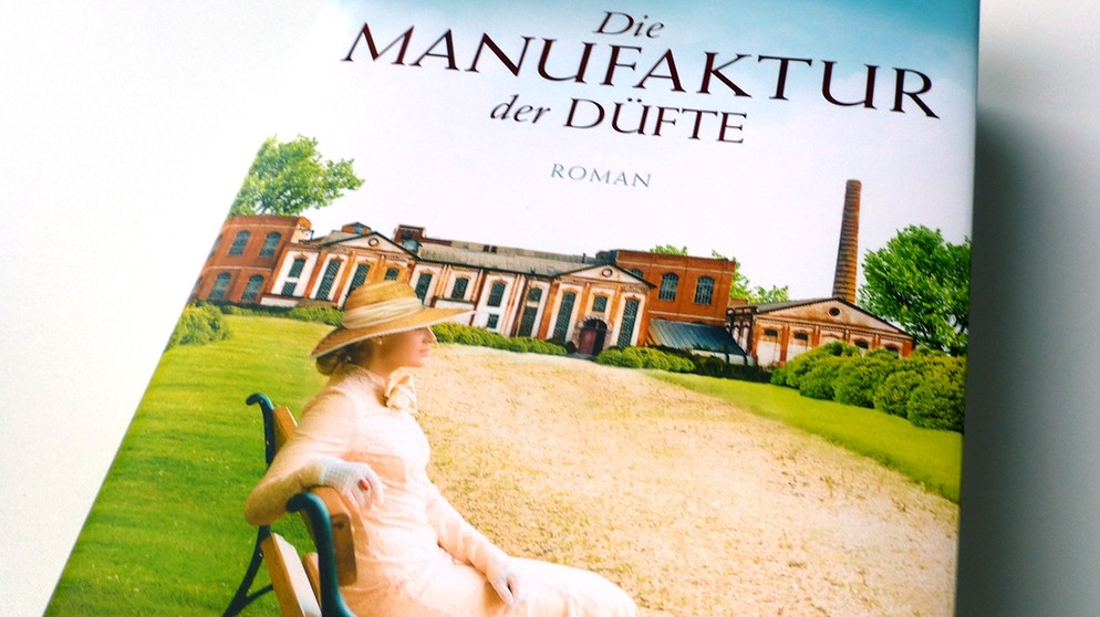 Cover des Romans "Manufaktür der Düfte" auf dem eine Frau vor einer Fabrik sitzt. | Bild: BR