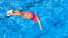 Eine Frau springt in den Pool eines Freibads. | Bild: mauritius-images